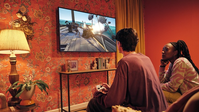 Two people on a couch in front of a Samsung smart TV playing Xbox cloud gaming with a controller.