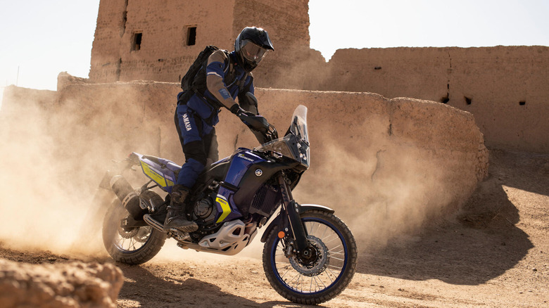 A side shot of a rider driving past a building in the desert on the Yamaha Tenere 700 World Raid.