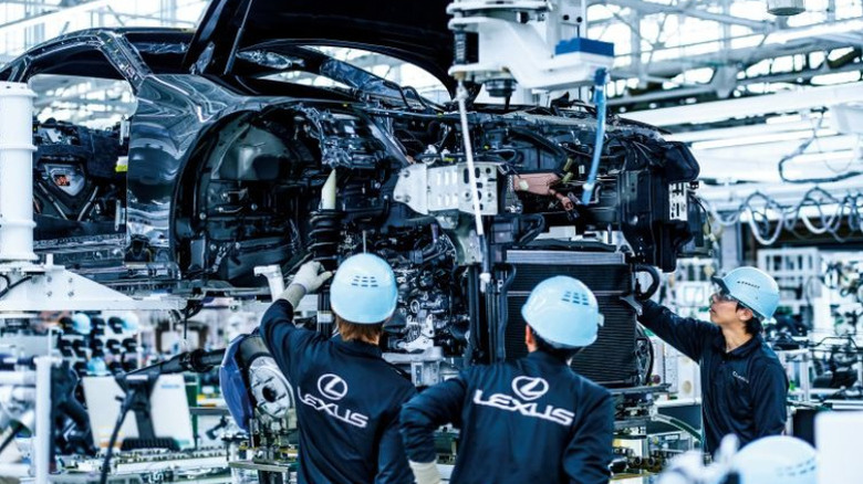 Workers wearing Lexus uniforms inspect work-in-progress Lexus car in factory