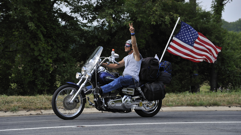 A biker riding a blue botorcycle with U.S. flag doing the biker wave