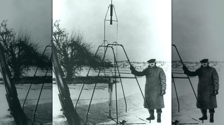 Dr. Robert H. Goddard standing beside his revolutionary rocket and frame