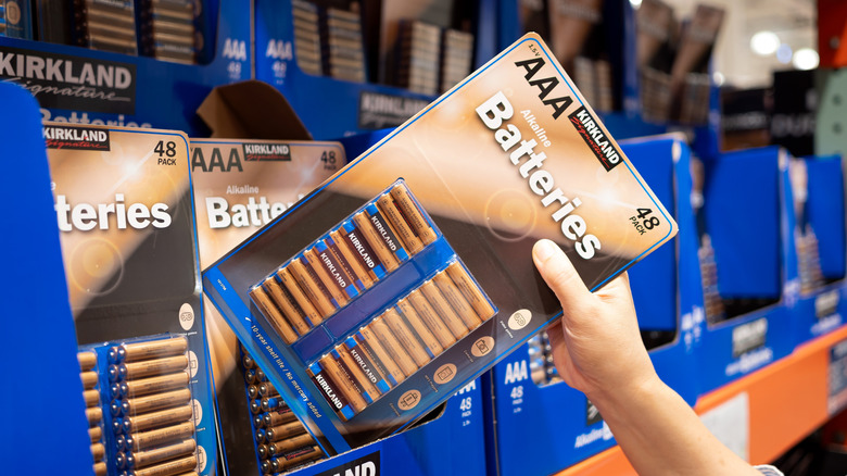 Hand pulling pack of Kirkland AA batteries from Costco store shelf display