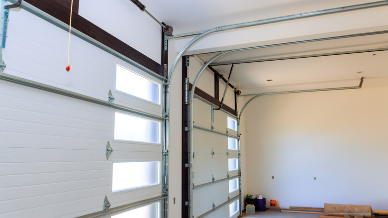 A roll-up garage door from the inside of a garage, white walls, random lumber on the floor
