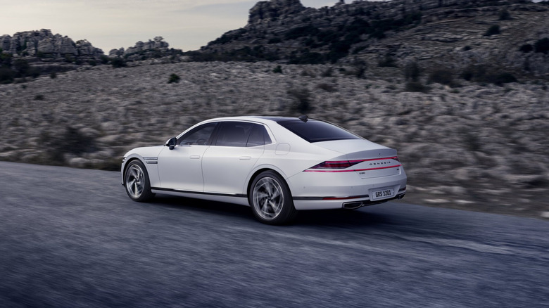 A white Genesis G90 on the move, rear 3/4 view