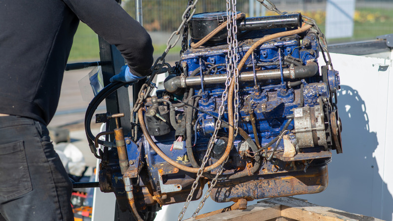 Mechanic places hand on engine suspended by engine hoist chains