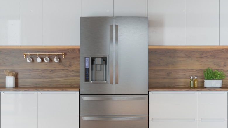 A large refridgerator with a water dispenser placed in the middle of a kitchen, hardwood walls and white cabinetry