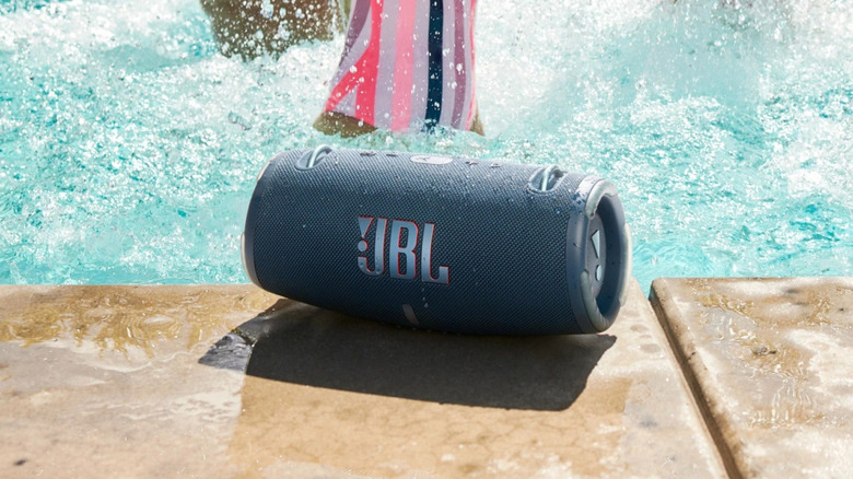 A water resistant JBL portable Bluetooth speaker by a swimming pool.