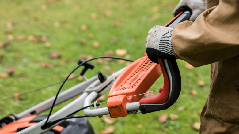 A close-up of the top of a lawnmower with gloved hands steering