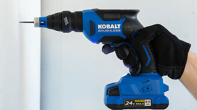 blue Kobalt cordless drill drilling into wall with black gloved hand