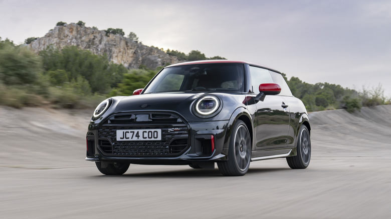 A Mini Cooper hatchback driving on open roads with mountains in the background.