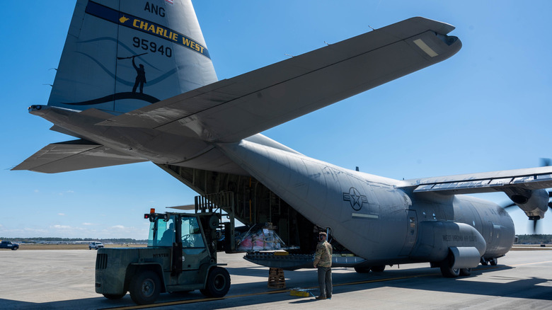 C-130 sitting on a runway, being loaded from behind with supplies