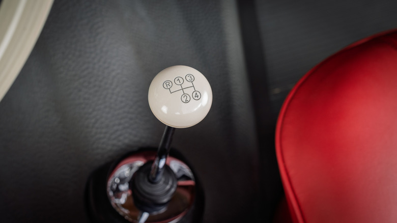 Top-down view of a white four-speed shift knob next to a red seat