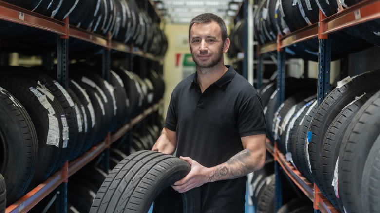 A mechanic is holding a tire in a storage row full of tires.