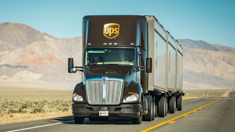 Front 3/4 view of UPS semi-truck with 3 trailers on highway in desert setting