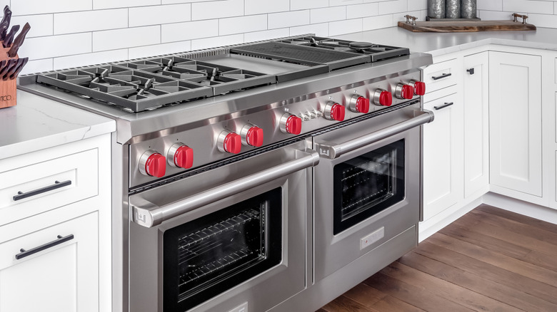 Close-up of stainless steel Wolf ovens next to white cupboards backgrounded by white subway tile.