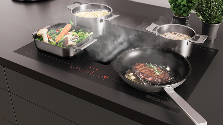 A Bosch cooktop installed on a dark countertop with pots and pans of food cooking