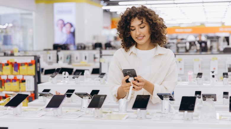 Customer comparing various smartphones while shopping in a consumer electronics retail store.