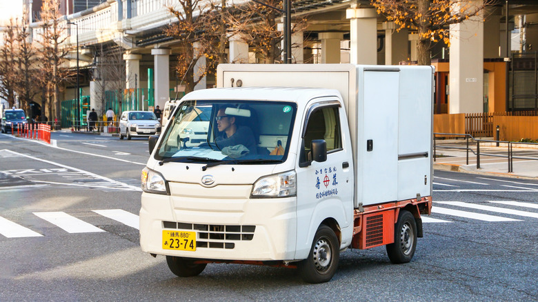 White Daihatsu HiJet mini truck cornering in a city