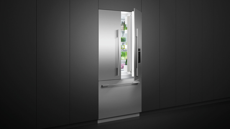 A stainless steel Fisher & Paykel refrigerator illuminating a dark gray kitchen with its open door