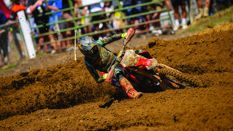 A dirt biker on a red GasGas bike cuts a corner on a muddy trail