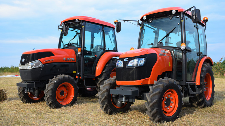 Two orange Kubota tractors in a field, front 3/4 view