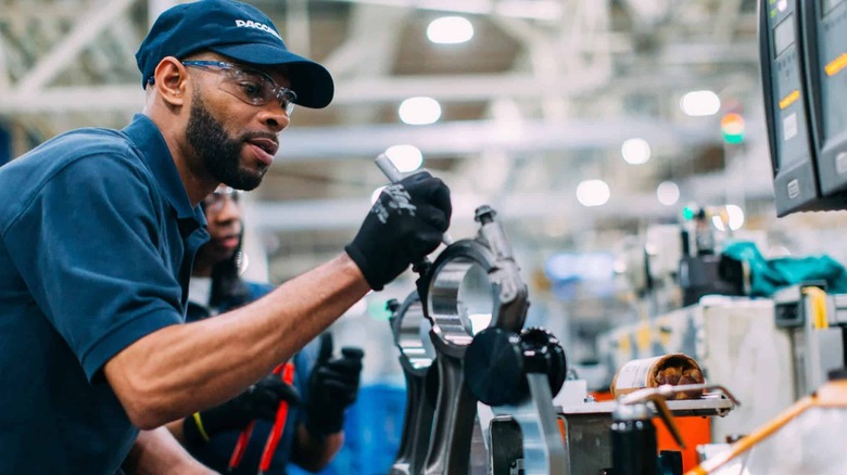 Worker wearing PACCAR uniform working on an engine on the assembly line