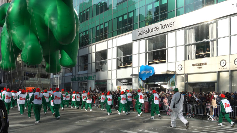 Sinclair's DINO at a Macy's Thanksgiving Day Parade, being held by a few people in DINO outfits
