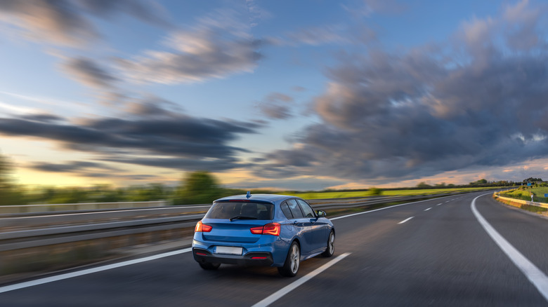 Rear view of a blue hatchback driving on an open highway