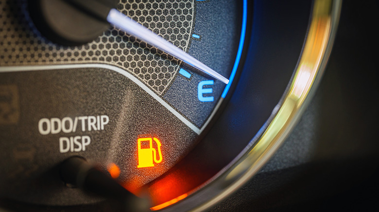 A car's fuel gauge showing nearly empty with the fuel warning light illuminated