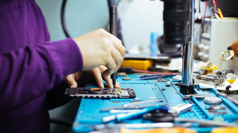 Technician disassembling smartphone with screwdriver