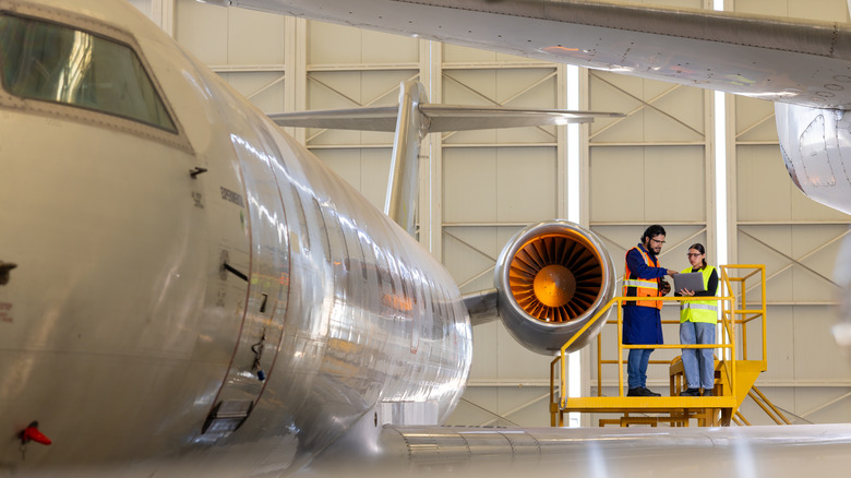 Two engineers inspect the fuselage of a passenger jet