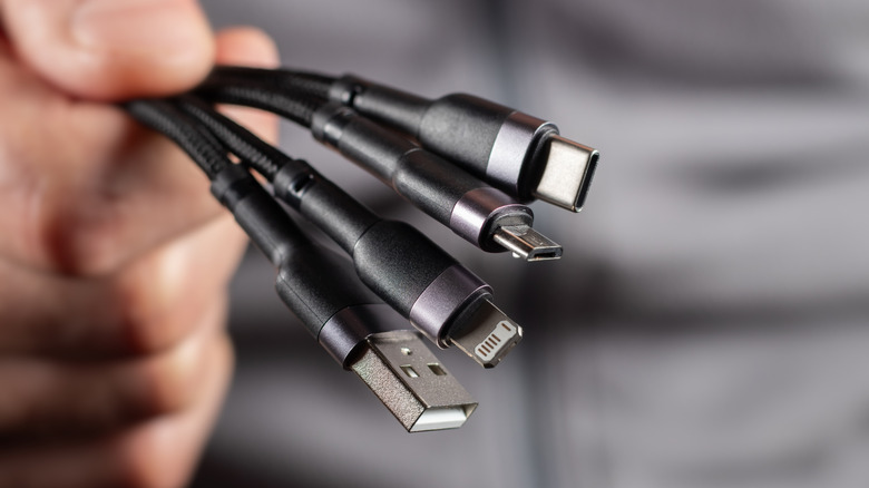The hand holds a universal USB cable. USB Type C, Micro USB, Usb lightning