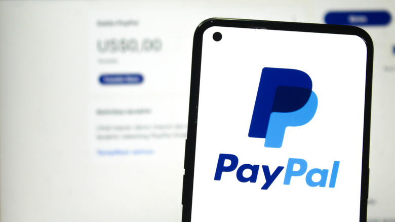 PayPal logo on phone screen with PayPal account website in the background.