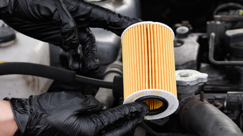 Close-up of mechanic wearing gloves holding a paper cartridge-type oil filter