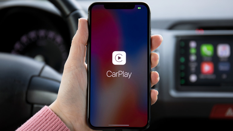 A woman's hand holding iPhone X with CarPlay on the screen in the car.