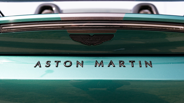 Aston Martin brand and logo behind a Vantage V8 convertible.