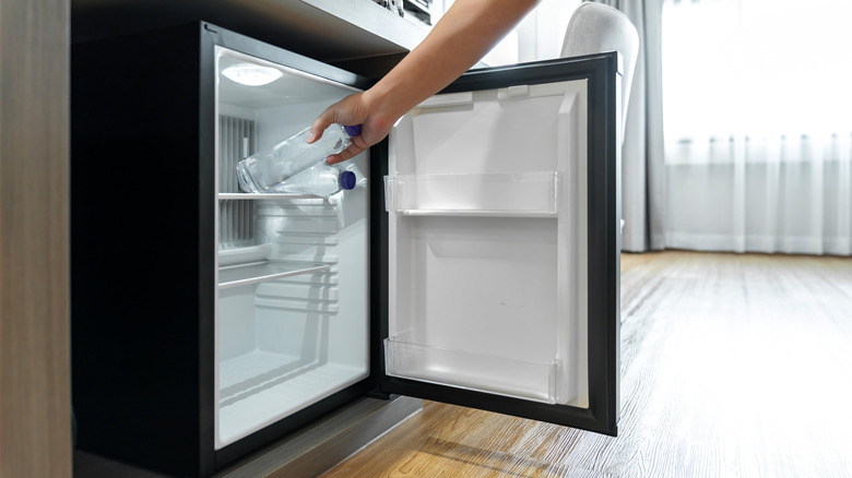 A person opens a tiny fridge in a hotel room