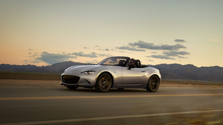 Silver Mazda Miata driving on the road with the top down.