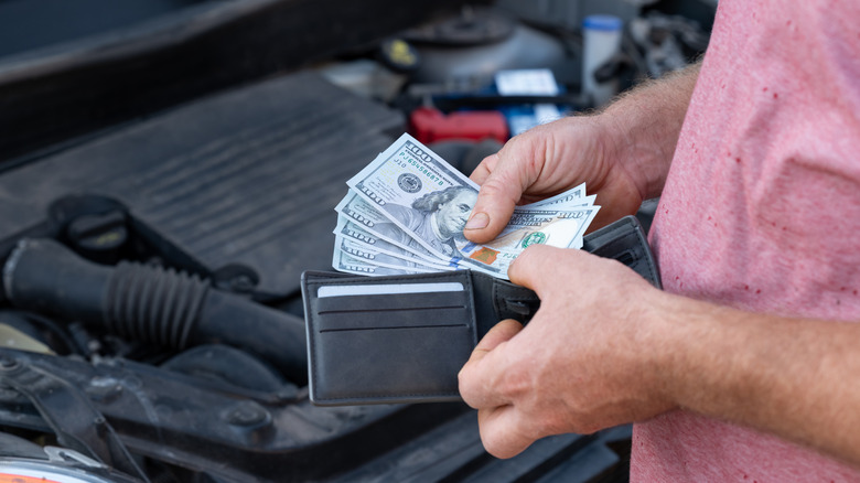A person pulling out cash from their wallet, vehicle's engine in the background