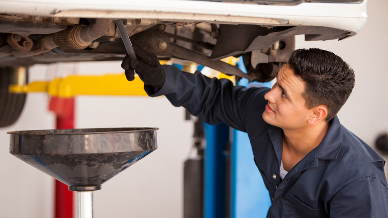 A technician draining oil from a vehicle that raised up on a lift