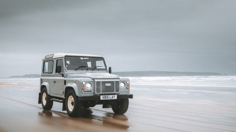 A front 3/4 shot of a classic Land Rover Defender 90 in baby blue driving on the beach.