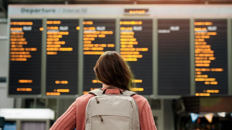 A woman looks at the flight schedule board at the airport with nothing but a backpack