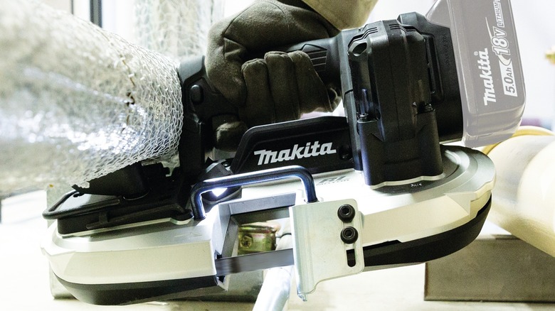 A person using a Makita subcompact band saw on tubing.