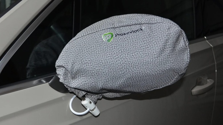A grey Prokevlock side mirror cover in place over a white car's side mirror. Only part of the car's side window and door is visible. The cover has the word Prokevlock on it and a green logo.