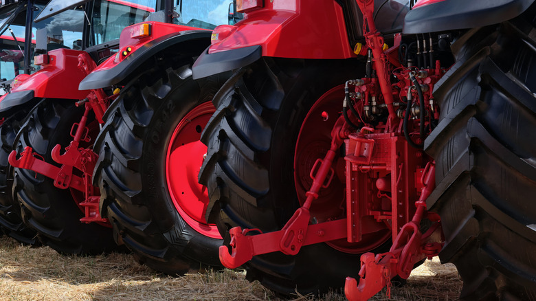 Rear view of several large modern red tractors standing in a field