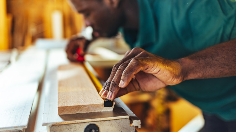 Man measuring out wood plank with tape measure