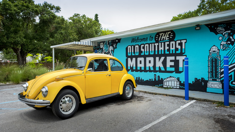 A vintage yellow car is parked in front of a revitalized food market in the historic neighborhood of Old Southeast in Saint Petersburg, Florida.
