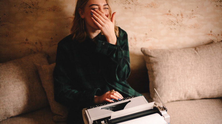 woman laughing while using typewriter on couch