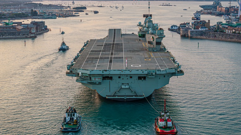 Arial view of aircraft carrier led by tug boats.