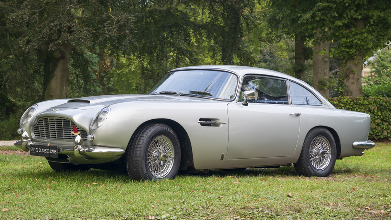 An Aston Martin DB5 Grand Tourer classic car on display in grass with trees in the background